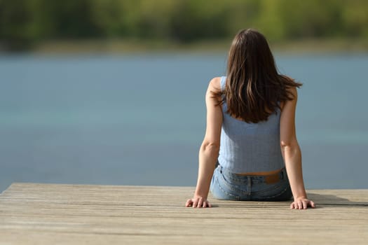 Back view of a woman sitting in a pier contemplating lake