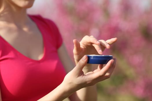 Woman hand in pink holding moisturizer jar in a field