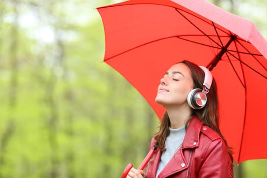 Woman holding umbrella listening to music in a park