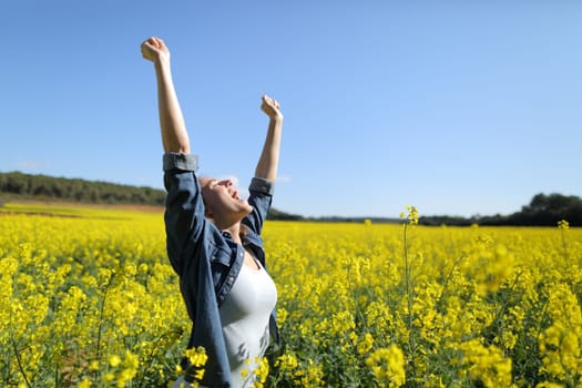 Excited female raising arms celebrating spring in a field