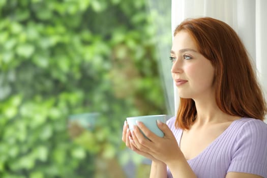 Woman looking through a window holding coffee mug