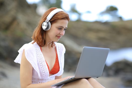 Tourist using a laptop with headphones on the beach