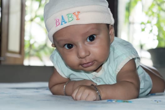 Cute baby lifting head. Closeup portrait. Happy baby boy looking and smiling at camera. Health care medical background. Sweet little infant toddler. Indian ethnicity. Developmental milestone for baby.