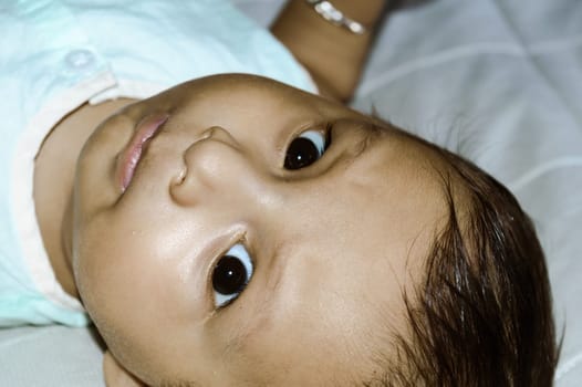 Close up face of cute newborn baby boy upside down and Looking at camera. Four month old Sweet little infant toddler Closeup portrait. Indian ethnicity. Front view. Child Health care background.