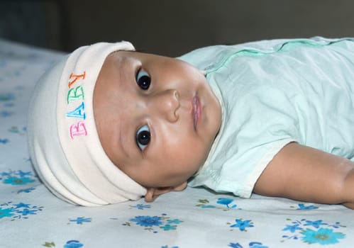 Upside down Closeup cute face of newborn baby boy lying on bed and Looking at camera. Sweet little infant toddler Closeup portrait. Indian ethnicity. Front view. Child Health care medical background.