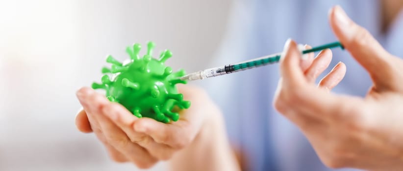 Medical worker holding a model of coronavirus and a syringe. Concept of vaccination aganst pandemic of Covid-19. Idea of fighting with pandemic.