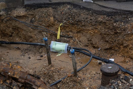 Dug up sidewalk revealing wires in protective tubes. Building of electric lines or telecommunication cables, construction of optical network connection. Excavation and maintenance