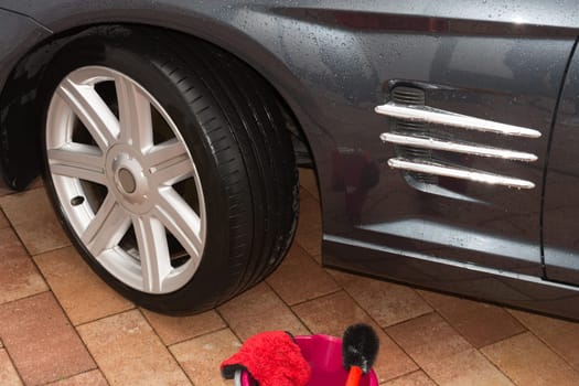 Car rims cleaning, car detailing wash concept. Cropped close up photo of male hand in black rubber glove with blue microfiber cloth washing car alloy wheel at car wash service