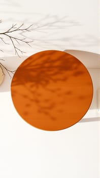 A simple wooden table with a round top filled with a coating that provides sunlight. The delicate shadows of leafy branches play on the textured cream wall in the background. High quality photo