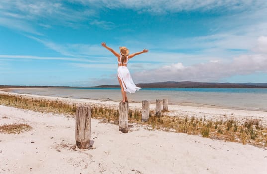 A woman throws her arms up over her head in sheer joy and zest for life on vacation by a beautiful beach setting in Australia