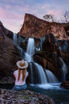 A woman sits by a beautiful mountain waterfall and rock pool