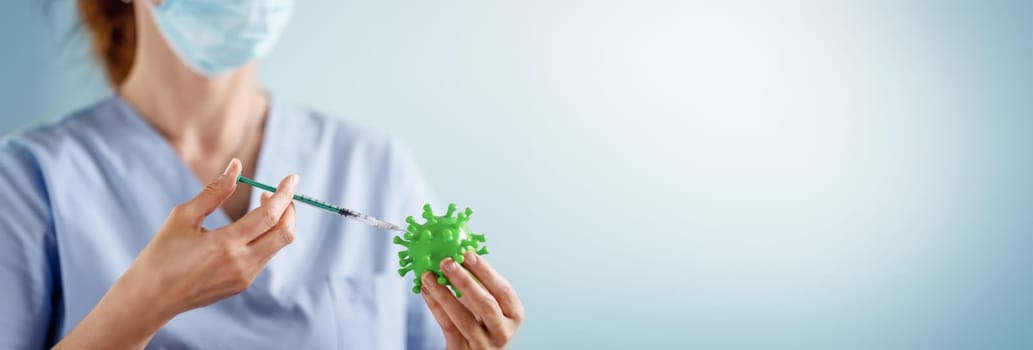 Medical worker holding a model of coronavirus and a syringe. Concept of vaccination aganst pandemic of Covid-19. Idea of fighting with pandemic.