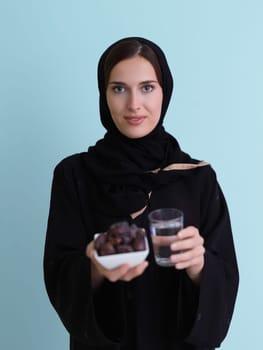 Modern muslim woman in abaya holding a date fruit and glass of water in front of her. Concept celebration of iftar time, end of fasting, in ramadan holy month