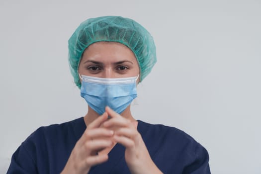 Close up of tired female doctor or scientist with a medical mask and surgical cap over grey background. Authentic real medical people hero in white in coronavirus pandemic is adjusting mask.