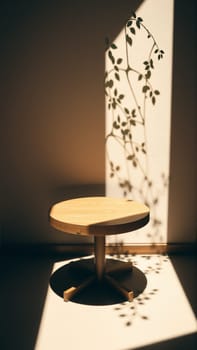A simple wooden table with a round top filled with a coating that provides sunlight. The delicate shadows of leafy branches play on the textured cream wall in the background. High quality photo