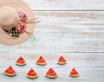 Flat lay of lady flowered straw hat and sliced watermelon tropical fruits on weathered white wooden background. Summer and holidays concept