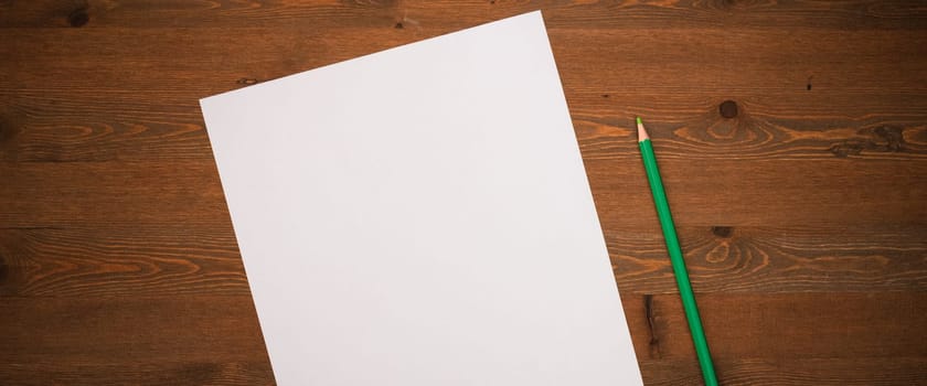 A blank white sheet and pencil for drawing on a wooden background with space for copying and lettering. Layout, mockup free space.