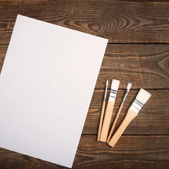 A clean white sheet and brushes on a textured background with space to copy. Layout, mockup space for text and drawing.
