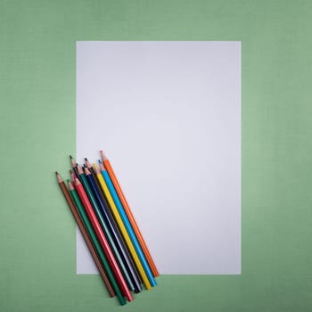 A blank white sheet and colored pencils for drawing on a plain textured background with space for copying and lettering. Layout, mockup free space.