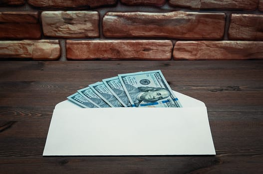 Dollars in one-hundred-dollar bills are spread out in an envelope on a table near the brick wall. Dollars fanned out. US dollars. On the envelope there is a place for an inscription, a logo. Color style. Layout, template, mockup.