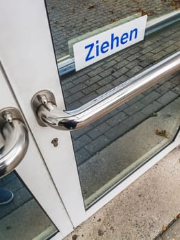 Elevated detail view of a locked shop door with a white sign and the words "Pull""."