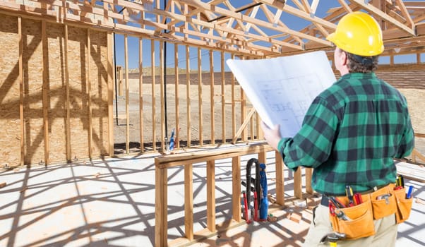 Contractor with hard Hat and Plans Standing Inside Construction Framing of New House.