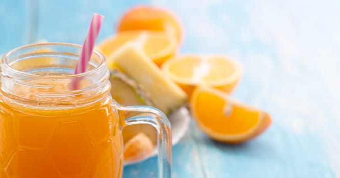 The glass vessel with the juice of orange with a straw on a blue table. Selective focus