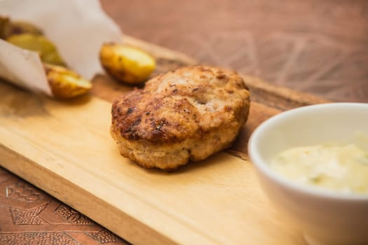 Succulent cooked beef burger with potato on a wood plate.
