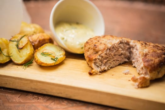 Succulent cooked beef burger with potato on a wood plate.