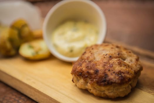 Succulent cooked beef burger with potato on a wood plate.