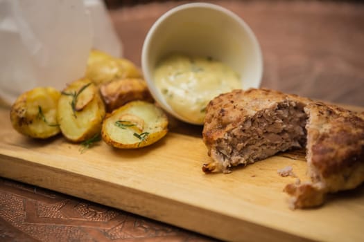 Succulent cooked beef burger with potato on a wood plate.