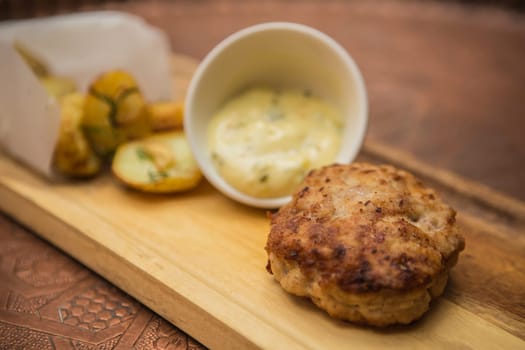 Succulent cooked beef burger with potato on a wood plate.