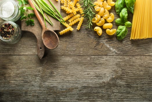 Pasta collection with herbs and spices on rustic wooden background