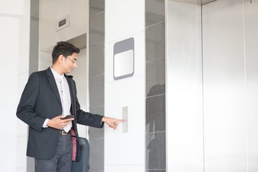 Young Indian businessman pressing on elevator button, waiting door open to enter inside the lift.