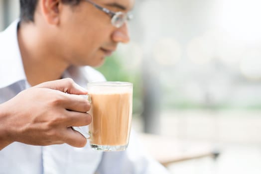 Asian Indian businessman holding a cup hot milk tea at cafeteria.