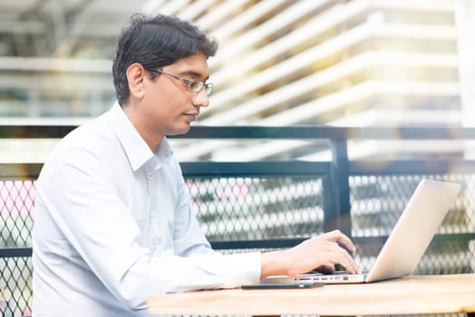 Candid Asian Indian businessman using laptop computer, modern building at background.