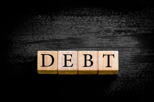 Word DEBT. Wooden small cubes with letters isolated on black background with copy space available. Concept image.