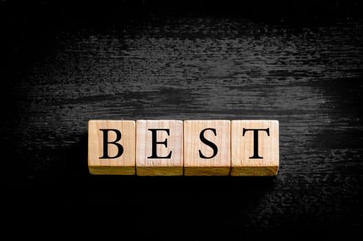 Word BEST. Wooden small cubes with letters isolated on black background with copy space available. Concept image.