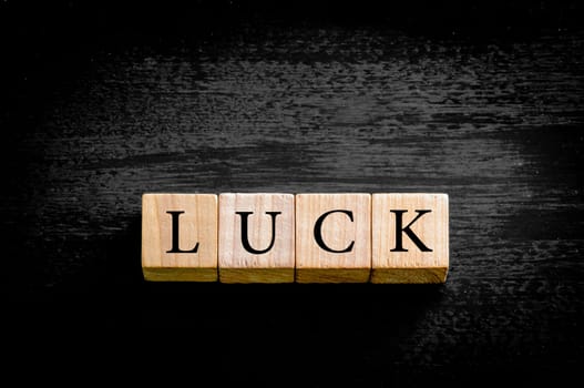 Word LUCK. Wooden small cubes with letters isolated on black background with copy space available. Concept image.