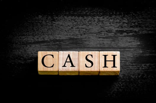 Word CASH. Wooden small cubes with letters isolated on black background with copy space available. Concept image.