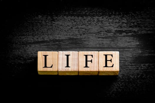 Word LIFE. Wooden small cubes with letters isolated on black background with copy space available. Concept image.