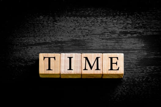 Word TIME. Wooden small cubes with letters isolated on black background with copy space available. Concept image.
