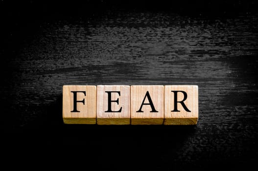 Word FEAR. Wooden small cubes with letters isolated on black background with copy space available. Concept image.