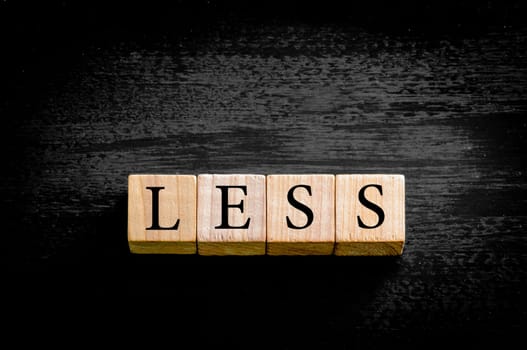 Word LESS. Wooden small cubes with letters isolated on black background with copy space available. Concept image.