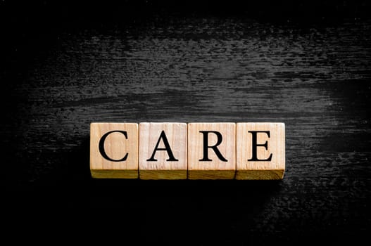 Word CARE. Wooden small cubes with letters isolated on black background with copy space available. Concept image.
