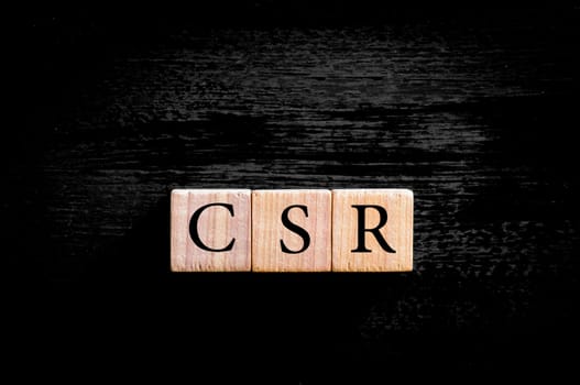 Acronym CSR- corporate social responsibility. Wooden small cubes with letters isolated on black background with copy space available.Business Concept image.