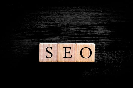 Acronym SEO - Search Engine Optimization. Wooden small cubes with letters isolated on black background with copy space available.Business Concept image.