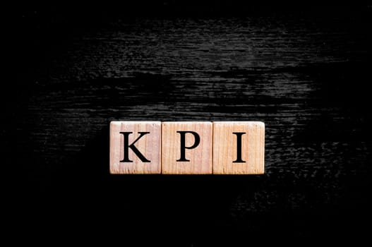 Acronym KPI - key performance indicator. Wooden small cubes with letters isolated on black background with copy space available. Business Concept image.