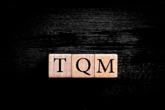 Acronym TQM - Total Quality Management. Wooden small cubes with letters isolated on black background with copy space available.Business Concept image.