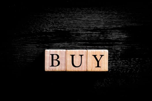 Word BUY. Wooden small cubes with letters isolated on black background with copy space available. Business Concept image.